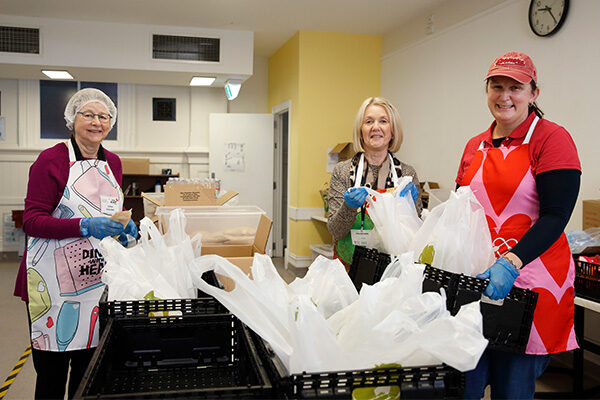 volunteers-preparing-takeaway-meals Three volunteers at the Dining Hall preparing takeaway meals