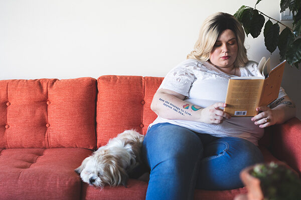 woman-sitting-on-couch-reading Woman sitting on a red couch with her dog and reading a bog