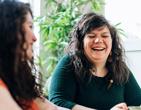 Two women siting next to each other, laughing
