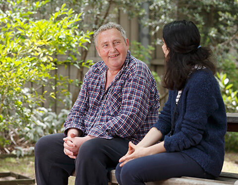 A client and a case manager talking to each other while sitting on a bench outside