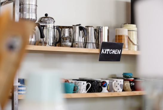 a shelf with a sign that reads 'kitchen', on the shelf are various silver coffee percolators and kettles