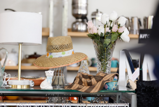 a straw hat, next to a white shaded lamp and random bric-a-brac items