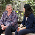 A man speaks to a woman on a bench outside