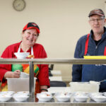 Two people preparing food in our Dining Hall and smiling into the camera
