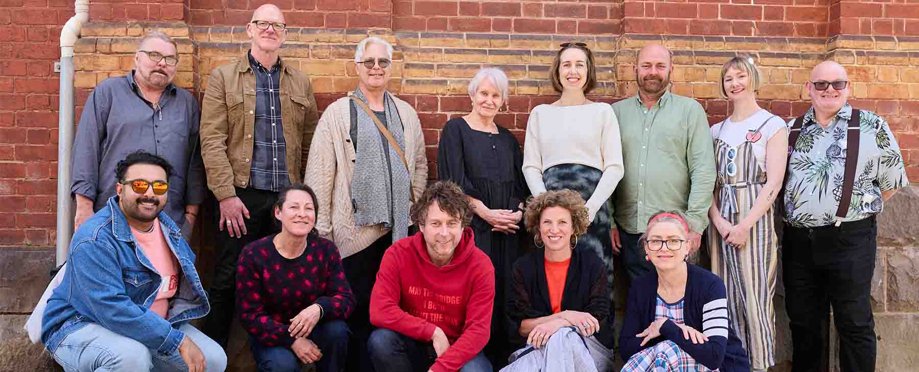 A large group of people some standing some kneeling in front of a brick wall