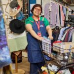 A volunteer in an op shop with a trolley of items for sale.