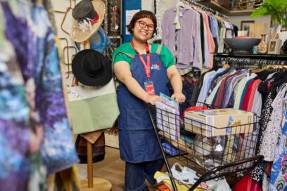 A volunteer in an op shop with a trolley of items for sale.