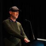 A man on a stage speaking at a lectern.