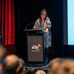 A woman standing at a lectern in front of an audience.