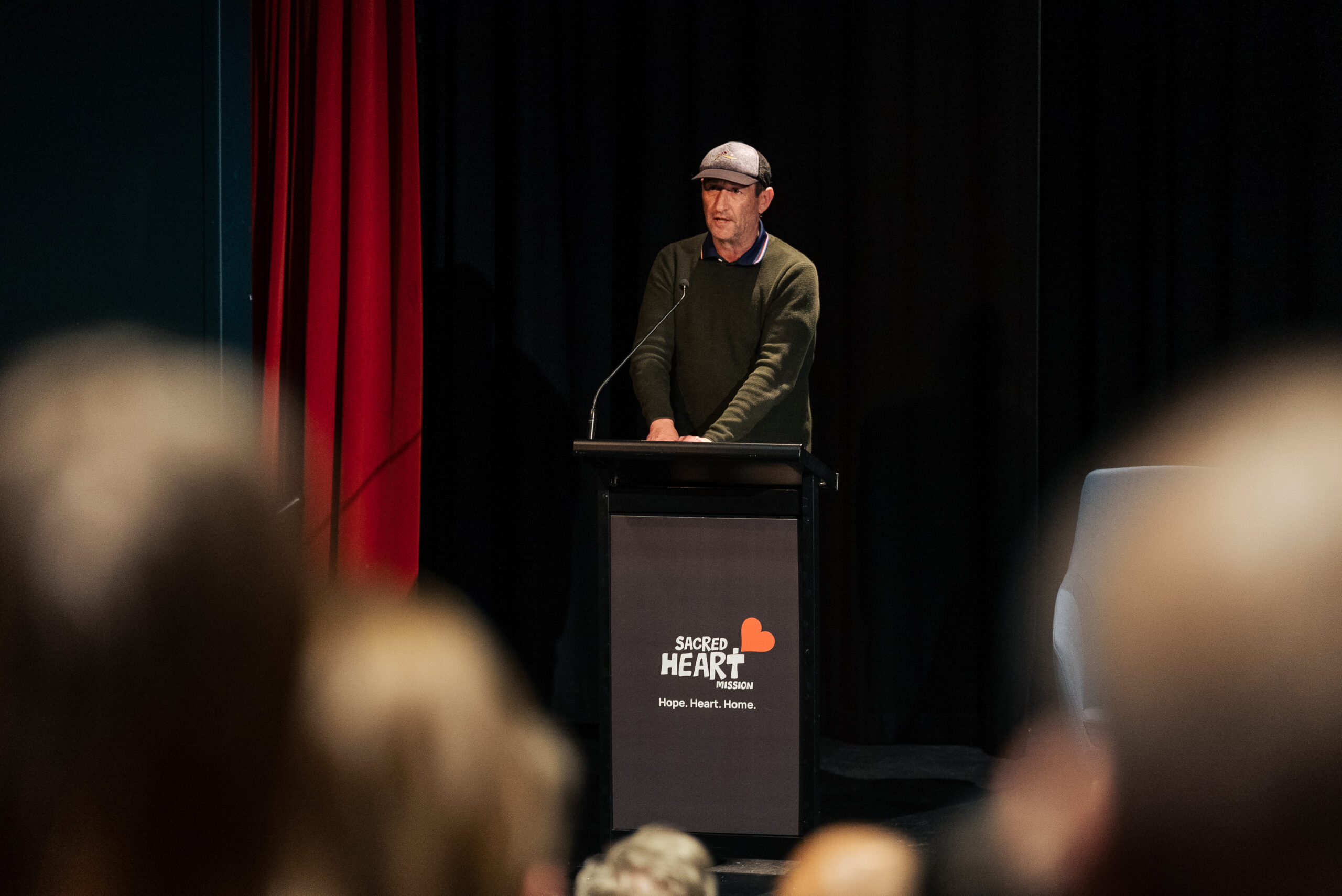 A man speaking at a lectern while an audience watches.